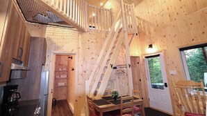 A wooden cabin interior with a kitchen, dining area, and a staircase leading to a loft.