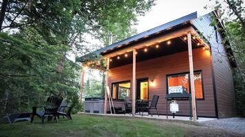 Enjoy a peaceful retreat in this cabin surrounded by a well-maintained lawn and trees, with a covered porch and outdoor cooking amenities.