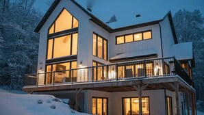 Kaksikerroksinen talo, jossa on suuret ikkunat ja parveke, ja sen ympärillä on lunta.