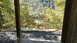 A view from a wooden structure with a concrete floor, overlooking a forested hillside. - Grandpa Dans Cabin+Mtn River view 34 acre retreat (Marshall)
