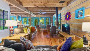 A cozy cabin interior with a wooden ceiling, a fireplace, a television, and a large window with a view of greenery. - Grandpa Dans Cabin+Mtn River view 34 acre retreat (Marshall)