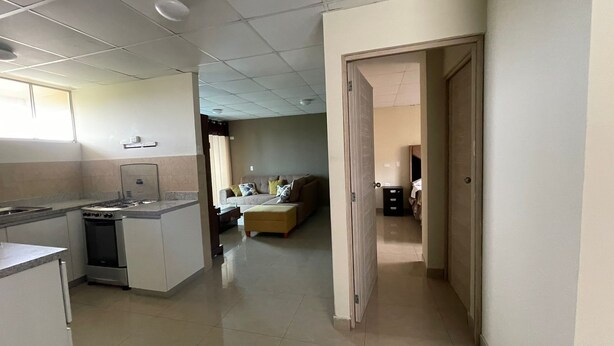 A spacious living area with a sofa, a dining table, and a kitchen area with a stove and cabinets. - Terrazas Suite (Lima)