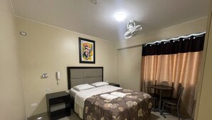 A hotel room with a bed, a desk, a chair, a small table, a ceiling fan, and a painting on the wall. - Terrazas Suite (Lima)