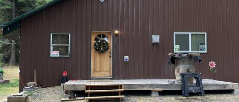 A brown metal building with a wooden door, a bench, and a small table with a flower.
