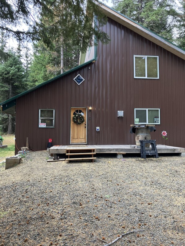 A brown metal building with a wooden door, a bench, and a small table with a flower. - Beautiful Cabin located in the Blue mountain’s, pet friendly and many extras. (Weston)