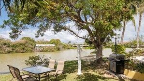 A lakeside patio with a table and chairs, a hammock, and a barbecue grill. - Spacious & Relaxing Mango Suite at Award-Winning Shangri-La Bed & Breakfast (West Bay)