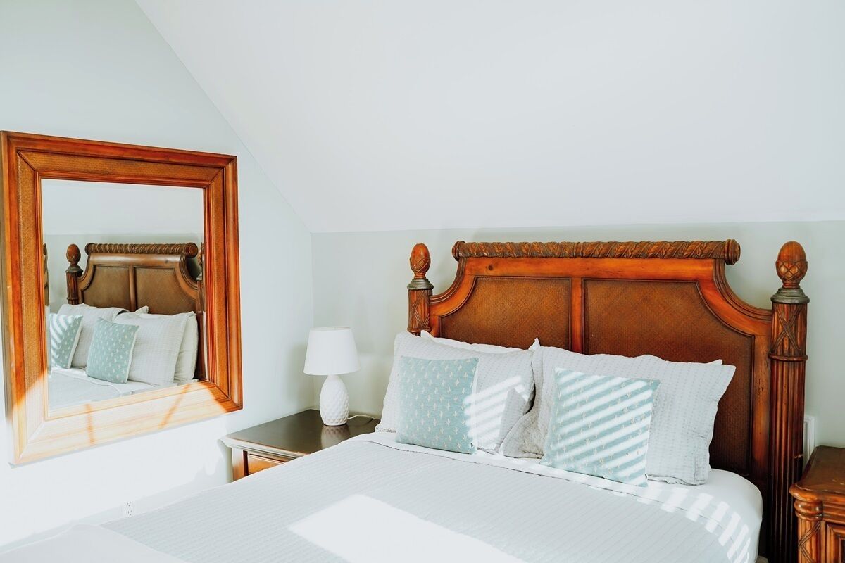 A neatly made bed with a wooden headboard, a bedside table with a lamp, and a large mirror on the wall.