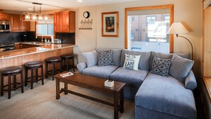 A modern living area with a kitchen, a grey sofa set, a wooden coffee table, and a bar stool arrangement. - Adrift - Unit 6 (Chelan)