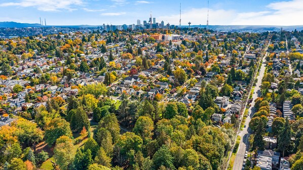 An aerial view of a residential area with houses, trees, and a distant city skyline.