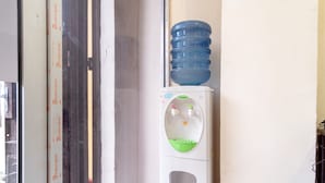 Een waterdispenser met een grote waterfles erop, een groene wasbak en een raam met een gedeeltelijk zichtbare deur.