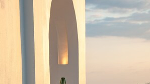 Una planta en test, en un test gran sobre un paviment de rajoles, un test més petit al fons, i un edifici amb una finestra apuntada.