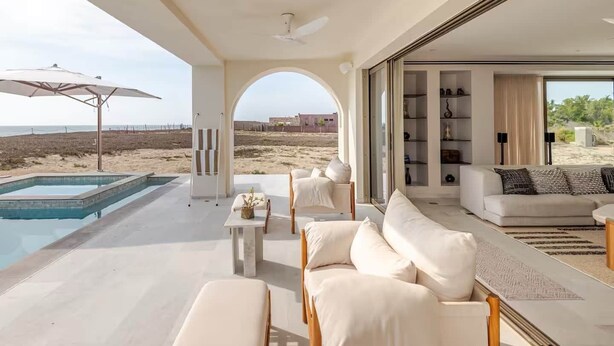 Zona d'estar moderna i oberta amb piscina, seients exteriors i vista a la platja.