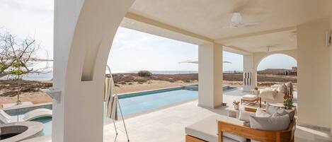 Un moderno espacio lounge al aire libre con piscina, asientos y vistas a la playa.