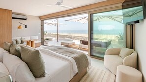 Un dormitori amb un llit gran, un sofà, un televisor i un balcó amb vista a la platja.