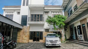 Un edificio de dos pisos con fachada blanca, un balcón en el piso superior y un coche estacionado al frente.