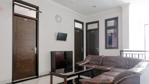 Una habitación con un amplio sofá de cuero, una mesa de centro de vidrio, un televisor y tres puertas de madera oscura.