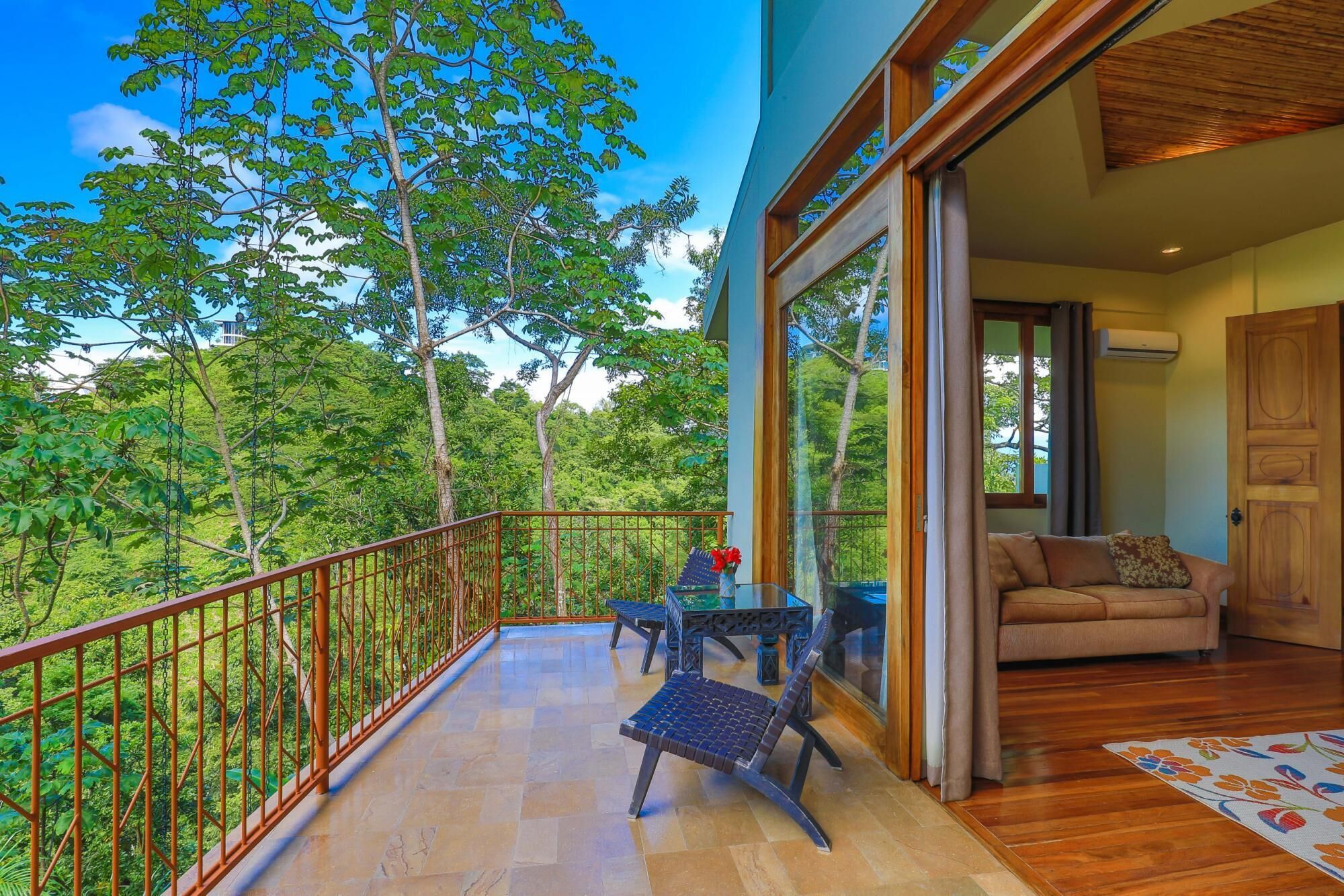 A balcony with a view of lush greenery, a wooden floor, and a sofa with cushions.