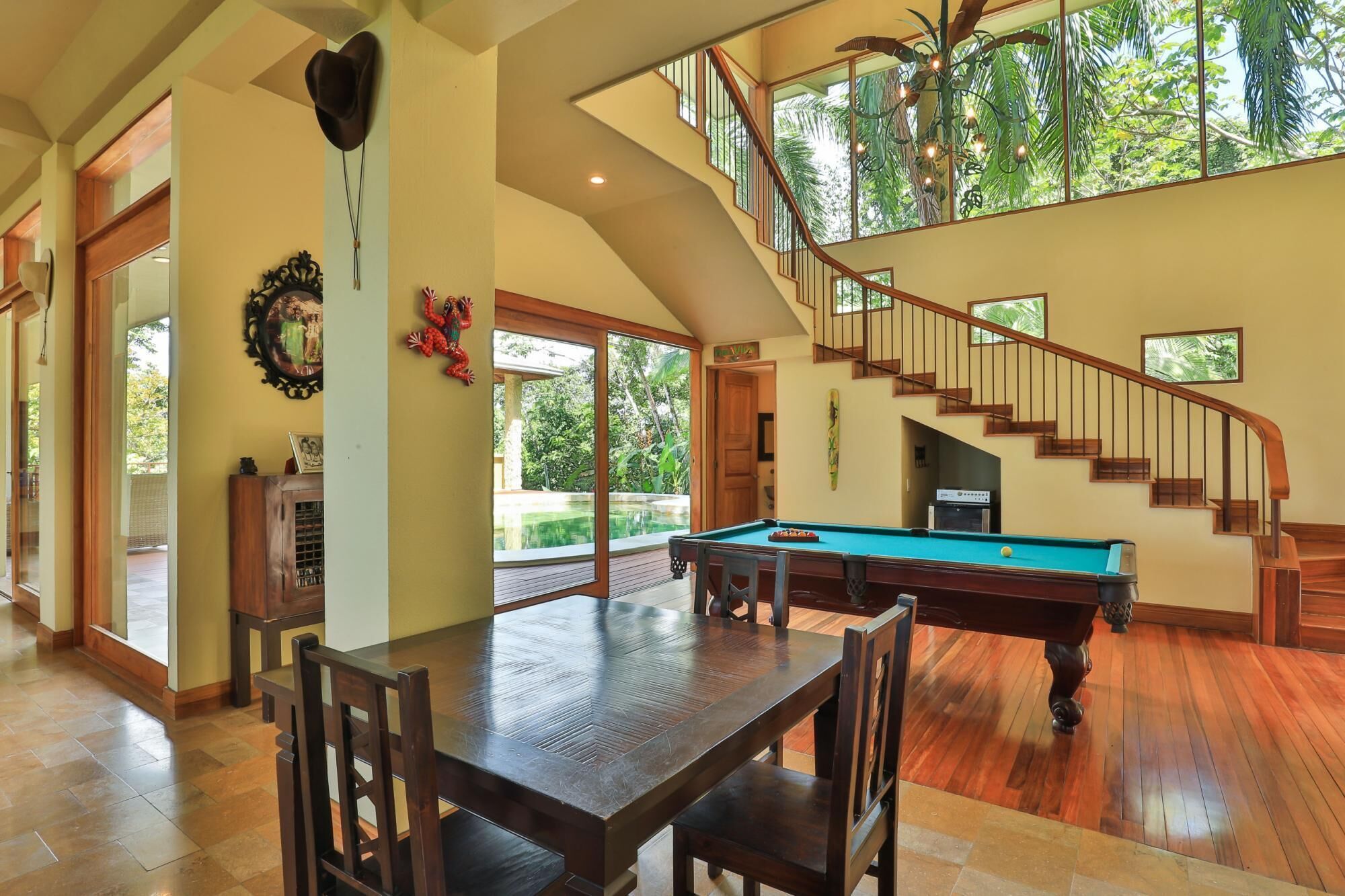 A spacious living area with a pool table, wooden flooring, and a staircase leading to an upper level.