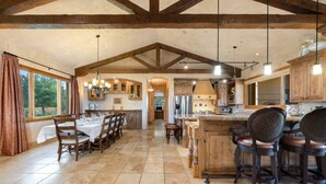 Una cocina amplia con vigas de madera, un comedor con mesa y sillas, y una barra con taburetes.