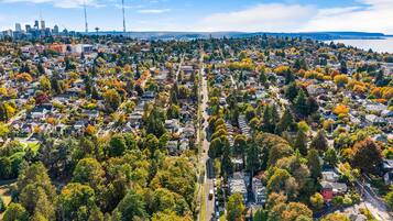 An aerial view of a residential area with houses, trees, and a distant city skyline.