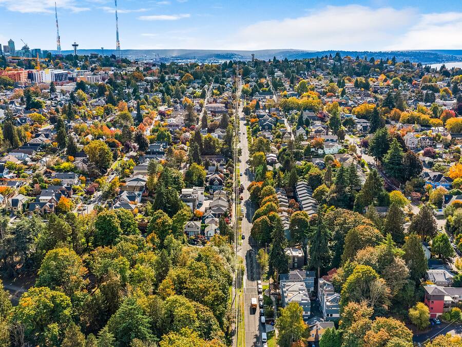 An aerial view of a residential area with houses, trees, and a distant city skyline.