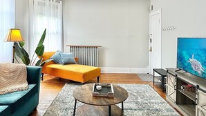 Uma sala de estar com sofá, mesa de centro, televisão e radiador.