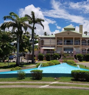 Stunning hotel facade with a central entrance, flanked by two wings, and a beautiful pool area surrounded by lush greenery.