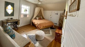A bedroom with a bed, a ceiling fan, a window, and a decorative wall piece.