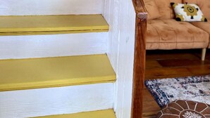 A staircase with white steps and yellow trim, leading to a room with a beige sofa and a patterned rug.