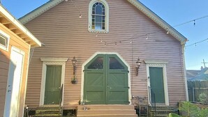A two-story building with a gabled roof, a central arched window, and a green door.