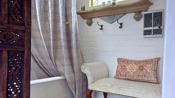 A room with a white bathtub, a wooden cabinet, a white chair, a round rug, and a window with a stained glass design.