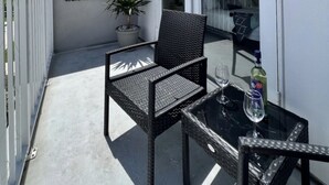 Un balcone con una sedia, un tavolo, una pianta in vaso e una bottiglia di alcolici.