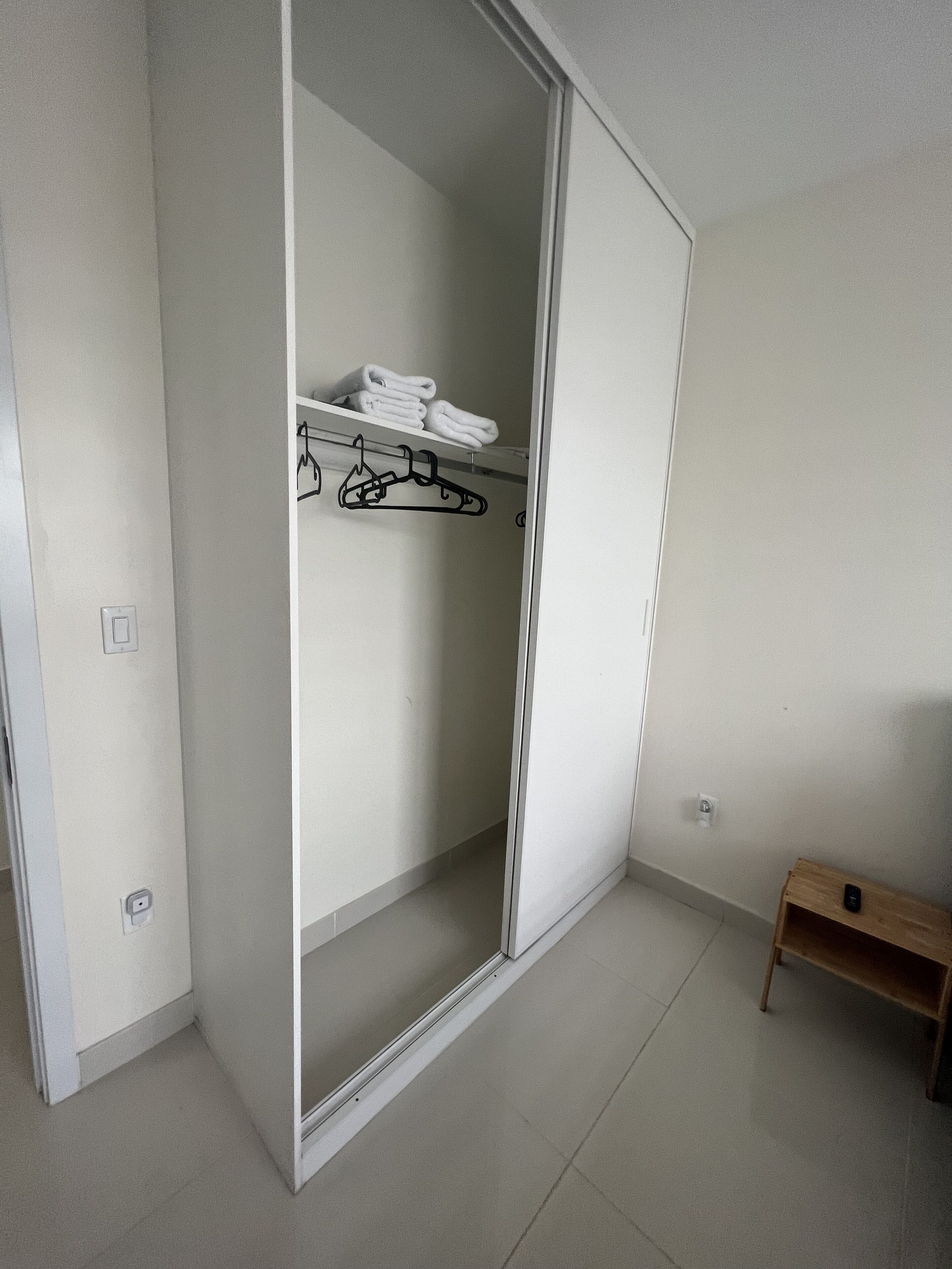 A walk-in closet with a sliding door, a shelf with folded towels, and a wooden bench.