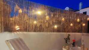 Ein Außenbereich mit Holztisch und -stühlen, einer dekorativen Bambuswand und Lichterketten.
