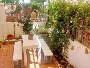 Un pati amb una taula blanca i bancs, envoltat de plantes en testos i una tanca de bambú.