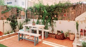 Un pati amb taula i bancs blancs, envoltat de verdura abundant i parets de bambú.