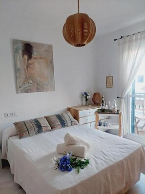 Un dormitori amb llit, una tauleta de nit, una làmpada penjant, un quadre i una finestra amb cortines.