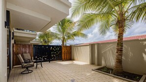 A patio with a palm tree, a wooden fence, and a chair. - Wariruri 1-14 BRAND NEW Apartment, private patio! (Noord)