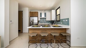 A modern kitchen with a central island, bar stools, and a view into the adjacent room. - Wariruri 1-14 BRAND NEW Apartment, private patio! (Noord)