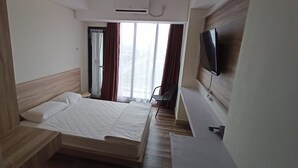 Una habitación de hotel con cama, televisor y ventana con cortinas.