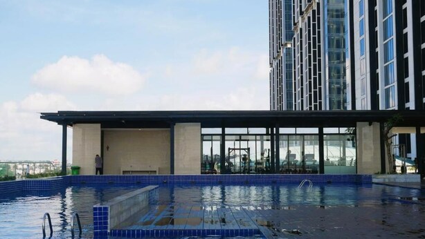 Una piscina en la azotea con cerramiento de cristal, una persona de pie junto a la piscina y un rascacielos al fondo.