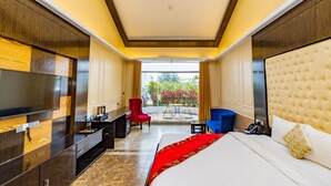 A hotel room with a large bed, a TV, a desk, and a chair. There is a view of a garden through a window. - Water Garden Resort & Spa (Tangail)