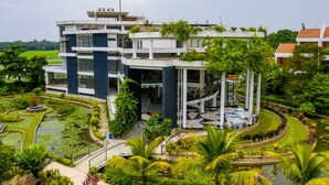 A modern multi-story building with a central atrium, surrounded by lush gardens and a small pond. - Water Garden Resort & Spa (Tangail)