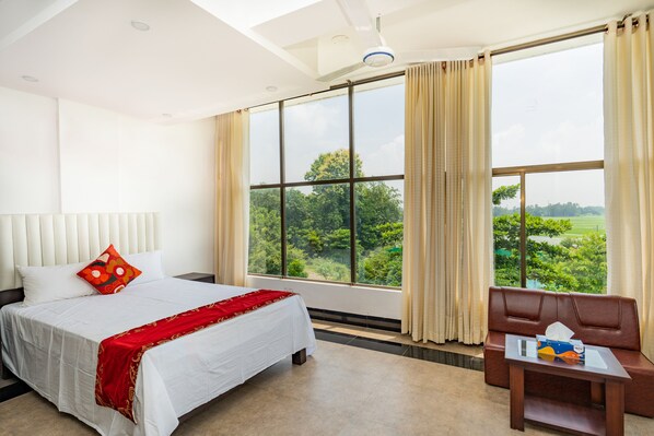 A hotel room with a large bed, a sofa, and a view of greenery outside.
