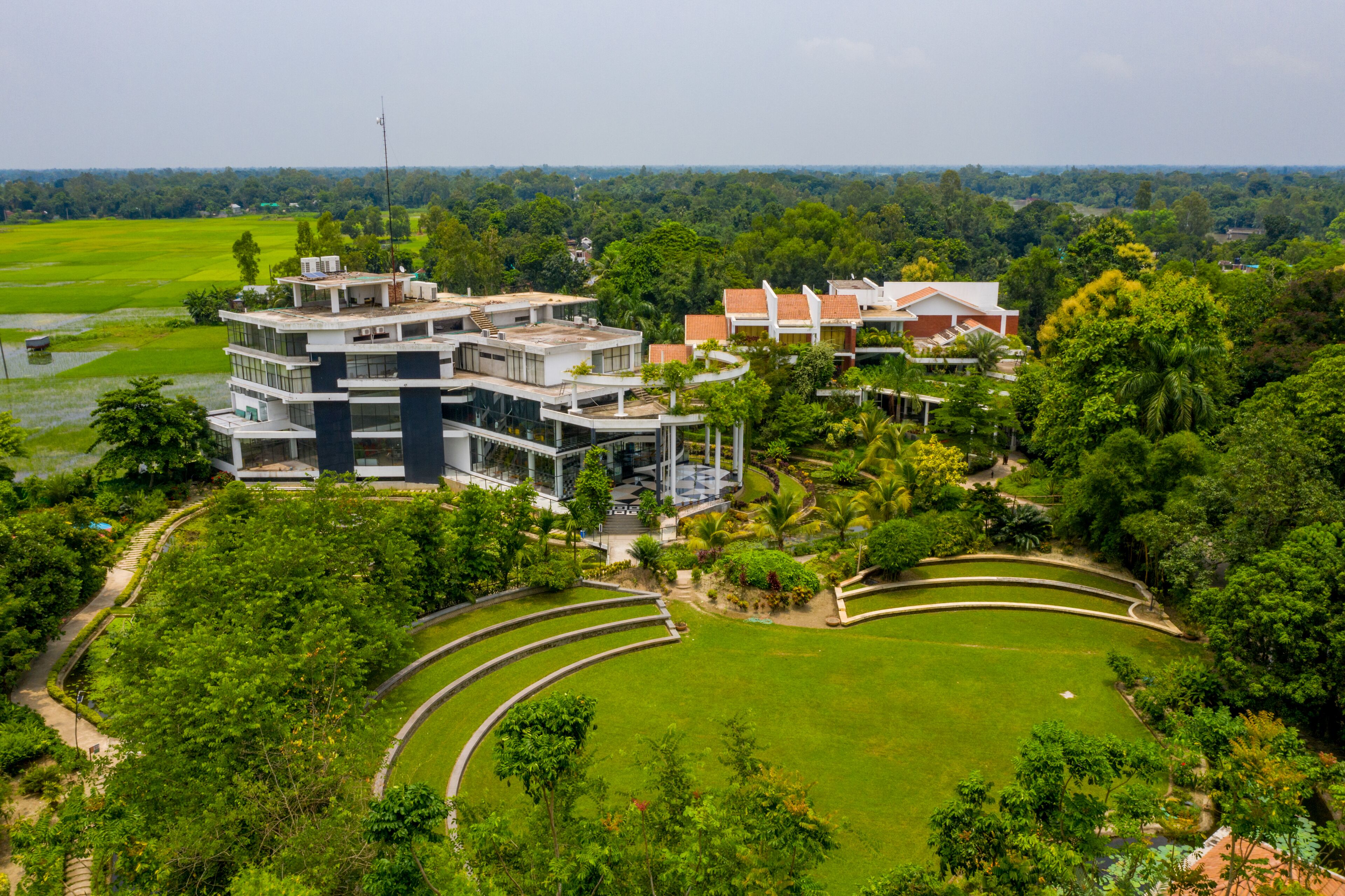 Um edifício moderno com vários andares, rodeado por vegetação exuberante e um gramado bem cuidado.