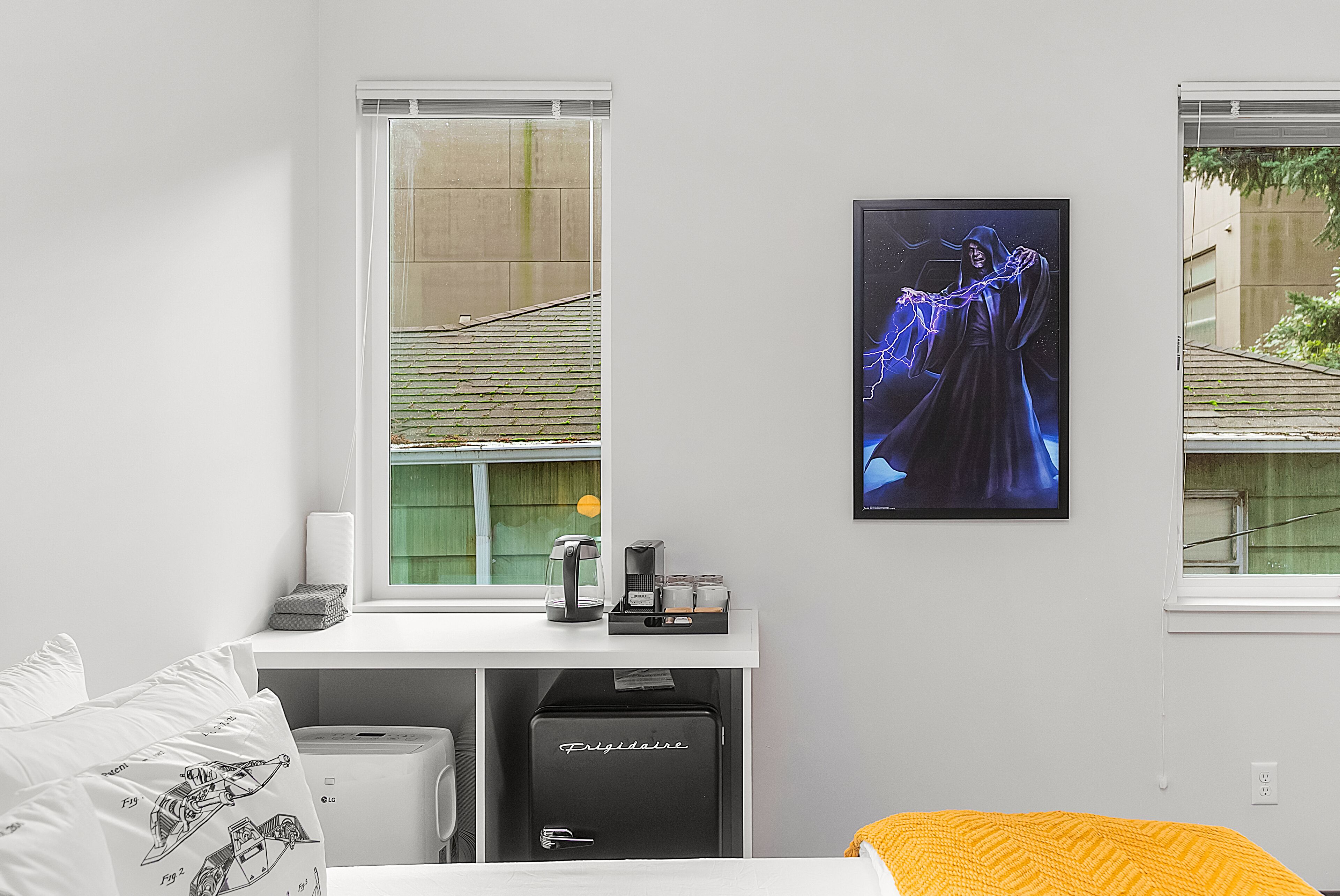 A hotel room with a bed, a desk with a computer, a printer, and a window with a view of buildings.