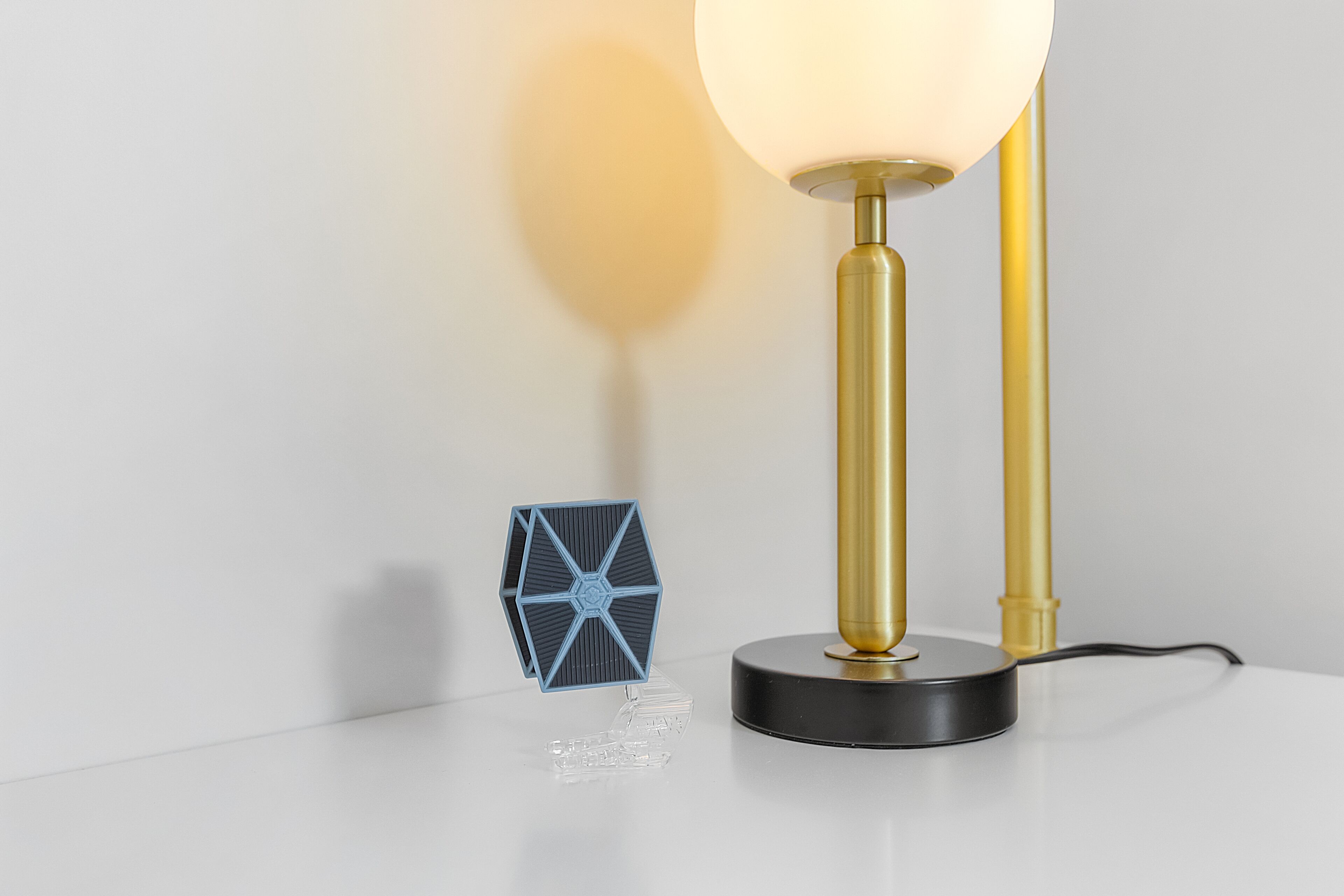 Una lámpara moderna con una base geométrica transparente y un soporte dorado.