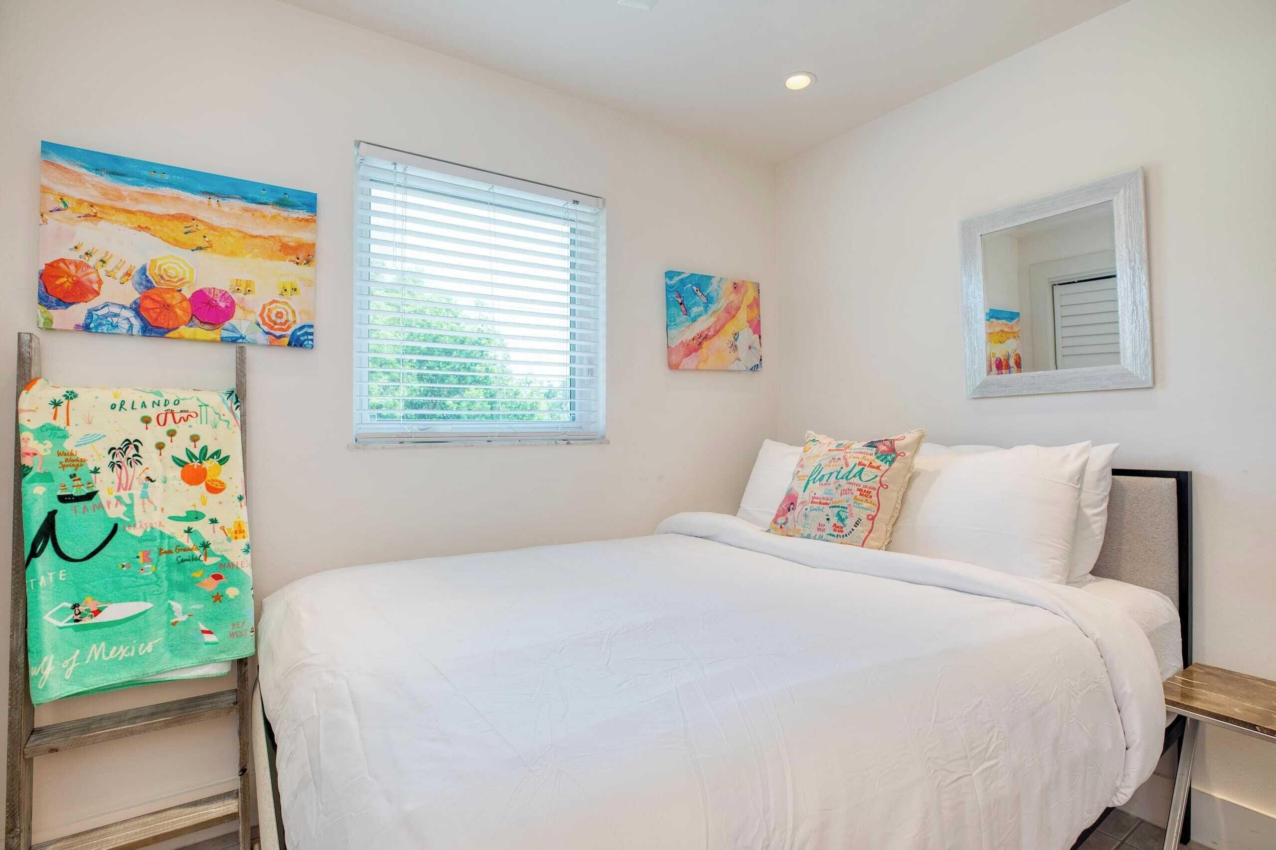 Un dormitorio con cama, una ventana con persianas y dos obras de arte colgadas en la pared.