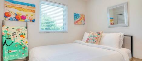 Un dormitorio con cama, una ventana con persianas y dos obras de arte colgadas en la pared.