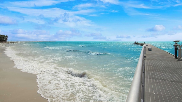 A beach with a wooden pier extending into the ocean, waves gently crashing onto the shore. - Sea Glass Secrets by Avantstay 3 Mins to Beach (Key West)